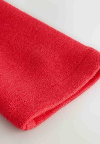 Punainen fleece-kangas käänteessä, jossa on pehmeä rakenne ja siisti ommel, neutraalia taustaa vasten.