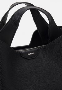 Svart skinn tote-veske med teksturert overflate, doble bærehåndtak, glidelåslukking og DKNY-logo.