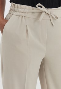 Beige broek met een structuurstof, elastische tailleband met een strik, en schuine zijzakken. Straight, relaxed fit ontwerp.