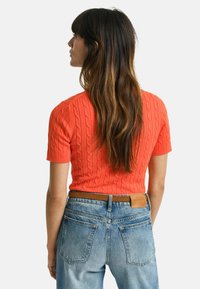 Kortærmet, kabelstrikket sweater i klar orange, parret med højtaljede lyseblå denim jeans med en brun bælte og label detalje.