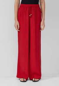 Pantalons larges rouges en tissu léger et texturé, avec une taille élastique et un cordon de serrage, ornés de perles en bois comme accents.