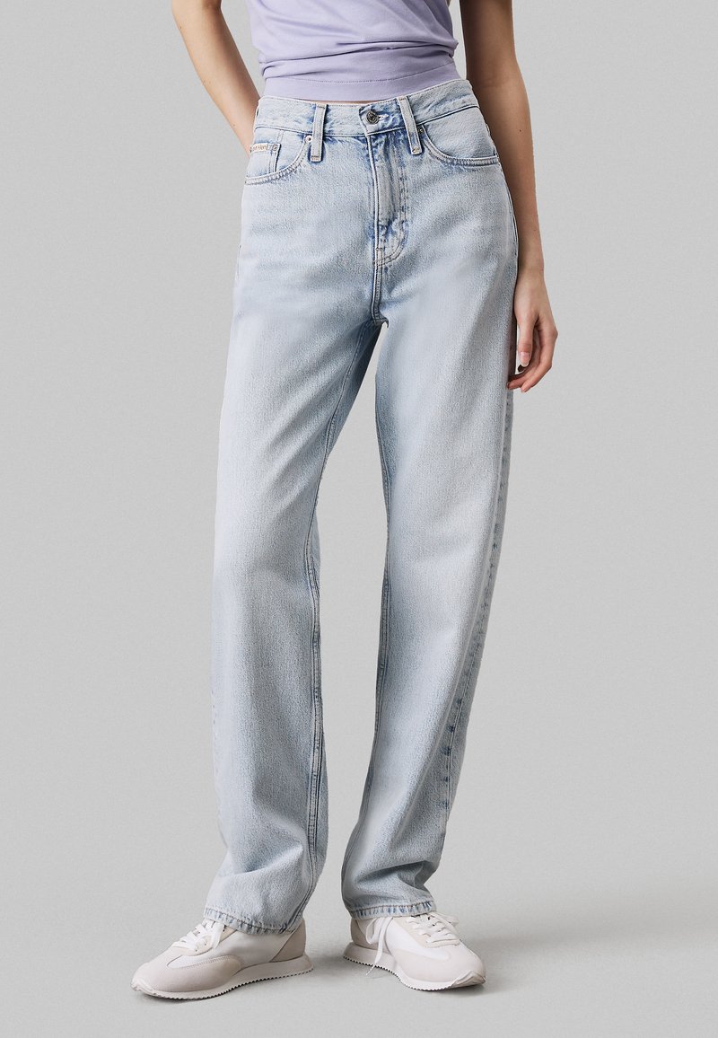 Jeans de mezclilla de tiro alto en azul claro con un diseño de pierna recta. Cuenta con cinco bolsillos y un desvanecimiento sutil. Combinados con zapatillas blancas.