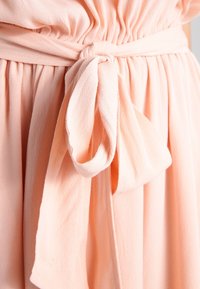 Pfirsichfarbiges Kleid aus Stoff mit gerafftem Oberteil und gebundenem Gürtel. Weicher, leichter Stoff mit gefältelten Details um die Taille.