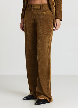 Braune Cordhosen mit weitem Bein und vertikaler Rippung, ausgestattet mit einem Knopfverschluss und Seitentaschen, kombiniert mit schwarzen spitzen Schuhen.