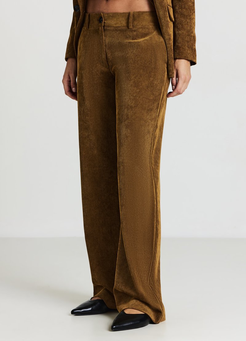 Braune Cordhosen mit weitem Bein und vertikaler Rippung, ausgestattet mit einem Knopfverschluss und Seitentaschen, kombiniert mit schwarzen spitzen Schuhen.