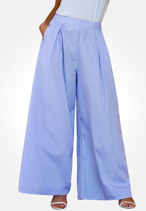 Woman wearing high-waist, wide-leg blue and white pinstriped pants with hands in pockets and white open-toe sandals.