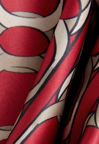 Tessuto rosso e beige con motivi che presentano cerchi e linee audaci, texture liscia e una finitura leggermente lucida.