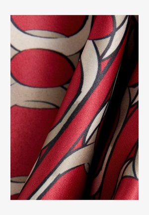 Red and beige patterned fabric featuring bold circles and lines, smooth texture, and a subtly glossy finish.