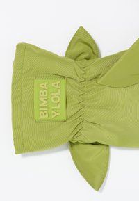Bolsa de nailon verde con textura fruncida, que presenta acentos puntiagudos y un parche de logo rectangular prominente que dice "BIMBA Y LOLO."