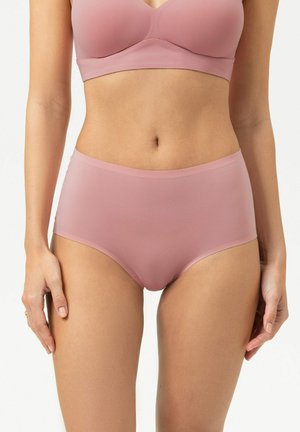 Woman wearing seamless mauve high-waist underwear and matching bra, standing against a plain light background.