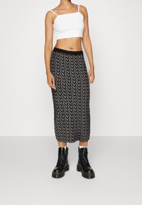 Vit linne topp med tunna band, kombinerad med en svart midikjol med ett vitt vågigt mönster, kompletterad med svarta snörda kängor.