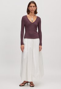 Langsleeve, getailleerde top van ribbelstof in pruimenpaarse kleur met een V-hals. Combinatie met een vloeiende witte maxirok met een gegolfde tailleband.