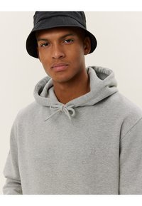 Gray hoodie made of soft cotton blend with a drawstring hood, featuring a small embossed logo on the chest and a relaxed fit. Black bucket hat worn.