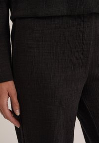Fekete, texturált nadrág, szőtt mintával, slim fit szabással és oldalzsebekkel. Anyaga láthatóan könnyű és enyhén gyűrött.