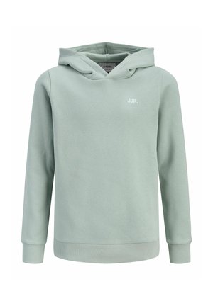 Dreng, der står med hænderne i lommerne iført en lysegrøn hættetrøje, matchende joggingbukser og hvide sneakers på en ensfarvet hvid baggrund.