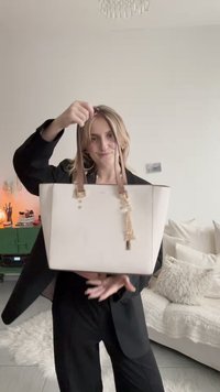 Vit tygpåse med bruna läderhandtag, en guldförsköning och en slät yta. Rektangulär form, minimalistisk design och utan synlig logotyp.