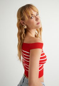 Czerwona, prążkowana bluzka off-the-shoulder z białymi paskami, zestawiona z wysokimi dżinsowymi szortami o teksturowanym wykończeniu i dopasowanym kroju.