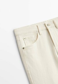 Jean en denim crème avec une coupe droite, présentant une poche avant, un bouton en métal et des coutures contrastées. Texture douce.