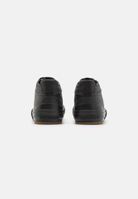Svart høytopp sneakers med en glatt syntetisk overdel, gummisåle og en bakheltapp for enkel påkledning. Subtil merking på siden.
