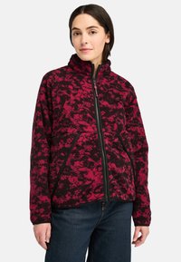 Giacca in pile con un motivo astratto rosso e nero, dotata di colletto alto, zip frontale e tasche laterali, caratterizzata da una texture resistente.