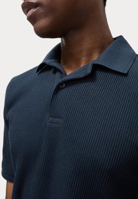 Polo de color azul marino texturizado con un diseño acanalado, que presenta un collar clásico y una tapeta de dos botones. Acabado de tejido suave.