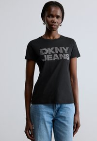 Svart t-skjorte i bomull med "DKNY JEANS" i hvite rhinsteiner, korte ermer og klassisk rund hals. Kombinert med lyseblå jeans.