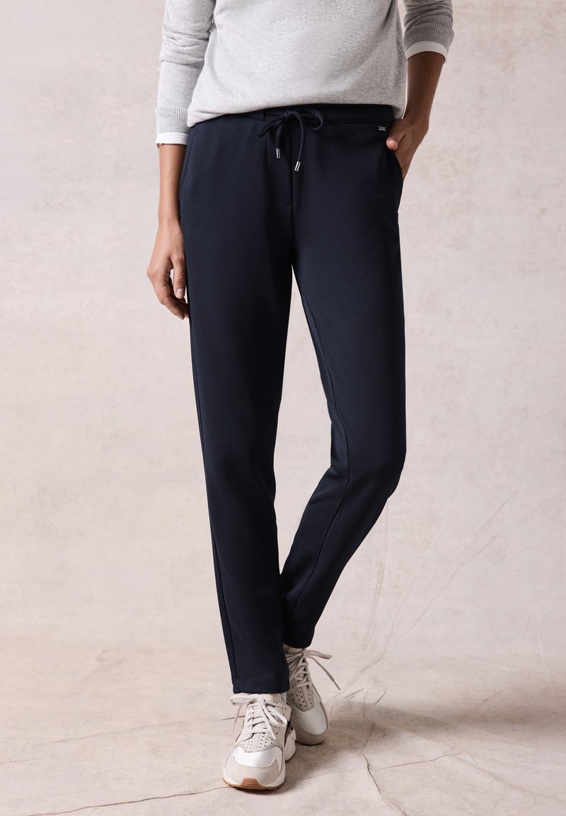 Marineblauwe sweatpants van zachte stof met een elastische tailleband, trekkoord, zijzakken en taps toelopende benen. Gepaard met een grijze gebreide trui en sneakers.