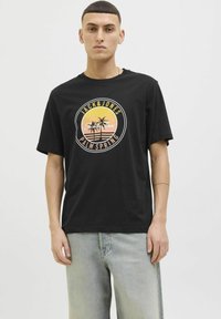 Camiseta de algodón negra con cuello redondo, que presenta un gráfico circular de una palmera en naranja y amarillo, con el texto "JACK & JONES" y "PALM SPRING".