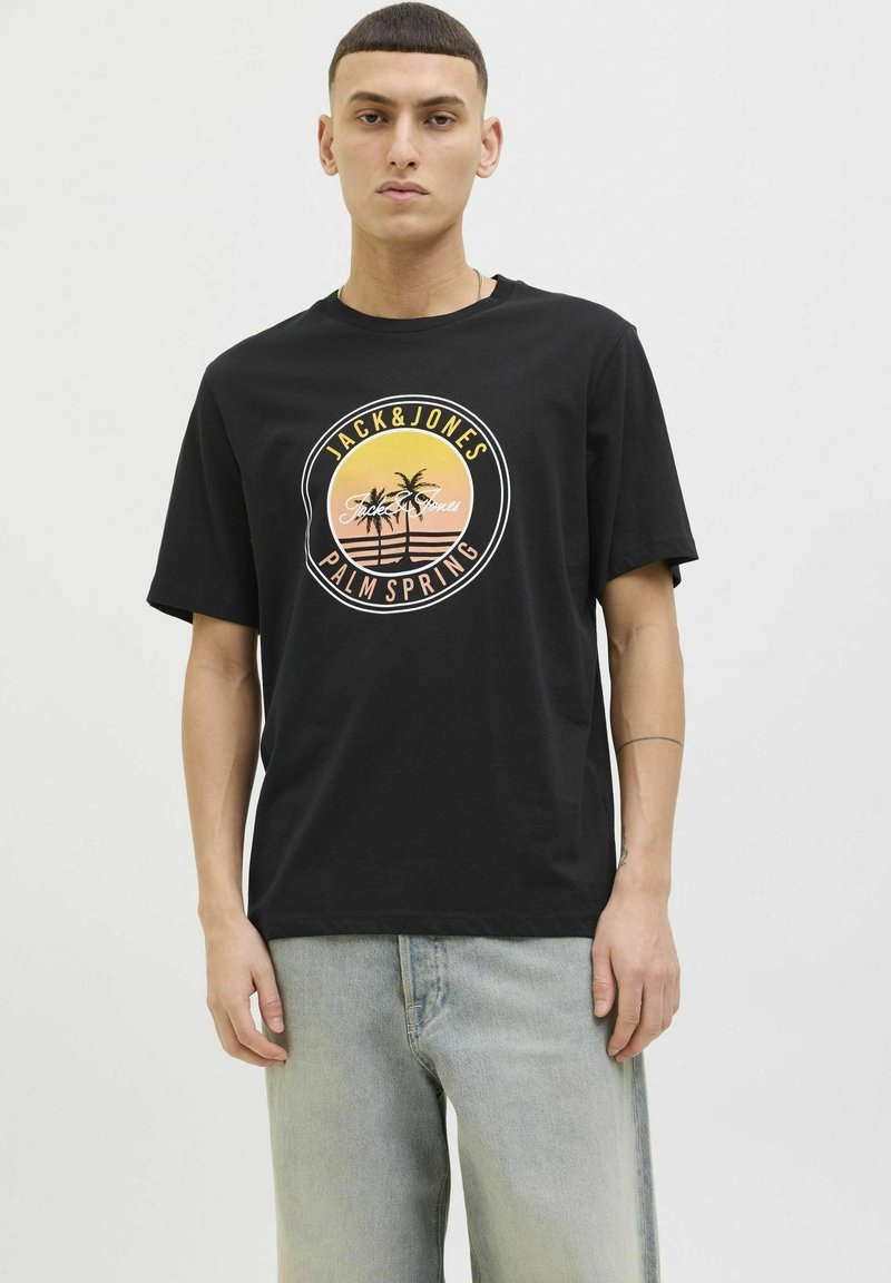 Musta puuvillapaita pyöreällä kaula-aukolla, jossa on ympyräinen palmupuun graafinen kuvasto oranssina ja keltaisena, sekä tekstit "JACK & JONES" ja "PALM SPRING".