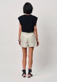 Zwart T-shirt met korte mouwen en geplooide schouderranden, gecombineerd met lichtgekleurde denimshorts met een elastische tailleband en twee achterzakken.