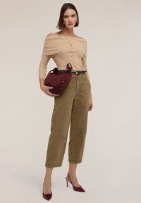 Suéter beige de canalé con los hombros al descubierto, pantalones cargo amplios verde olivo con bolsillos, bolso de ante burdeos y tacones puntiagudos burdeos.