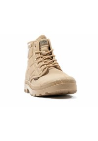 Botte montante beige avec tige texturée, bout rond et semelle profilée robuste. Présente un laçage à l'avant et un écusson en logo sur la languette.