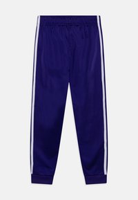 Pantalons de sport violets avec des rayures blanches sur les côtés, dotés d'une taille élastique et de poignets ajustés aux chevilles. Tissu lisse et extensible.