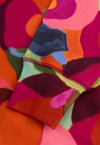 Multikleurige stof met abstracte vormen in roze, rood, oranje, paars en blauw. Naaddetails zijn uitgelicht, met een gladde, gestructureerde afwerking.