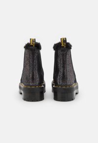 Black textured ankle boots with a glossy finish, faux fur trim, and chunky rubber soles. Yellow logo detail on pull tab.