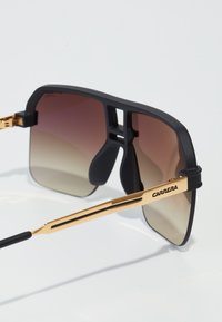 Ochelari Carrera negri și aurii cu lentile mari cu gradient, un cadru mat negru și accente din metal de culoare aurie elegante.