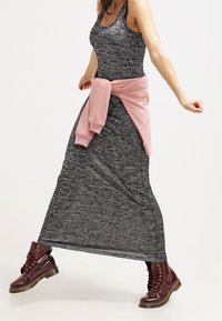 Šedé maxi šaty s pružným trupem a volnou sukní, doplněné o růžovou mikinu uvázanou kolem pasu a bordó šněrovací boty.