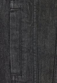 Svart denimtyg med en närbild av en ficka med synlig söm, som visar en mjuk textur och subtil glans.