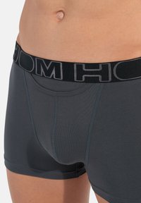 Tmavě šedé boxerkové trenýrky vyrobené z měkké tkaniny s černým elastickým pasem s vyvýšeným logem. Hladká textura s kontrastním stehem.