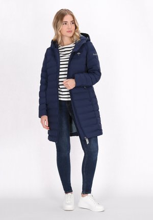 Navyblauwe pufferjas met een capuchon, voorzien van horizontale stiksels, een ritssluiting aan de voorkant, en gedragen over een zwart-wit gestreepte top en blauwe jeans.