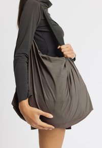 Person in dark long-sleeve top holds large, soft, dark gray shoulder bag with visible "rethinkit" logo on a plain light background.