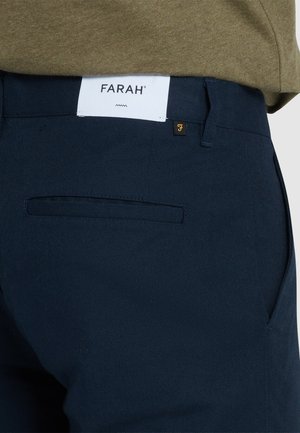 Pantaloni di cotone blu navy con superficie liscia, caratterizzati da una vita bianca con logo e una tasca posteriore con un elemento di design discreto.