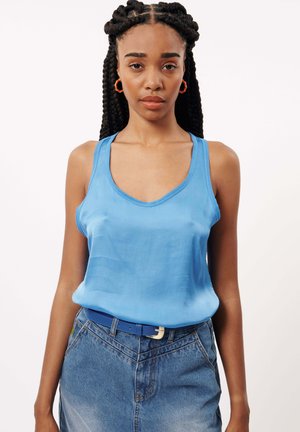 Top en satin bleu clair à encolure ronde, associé à une jupe en denim bleu. La tenue est complétée par une ceinture bleue avec une boucle dorée.