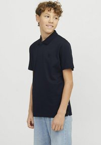 Mörkblå polo skjorta med strukturerad krage, korta ärmar och ett litet märke på bröstet. Bärs med ljusblå denimjeans.