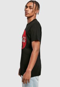 Sort bomulds t-shirt med et stort rødt Coca-Cola logo på fronten. Designet inkluderer en klassisk vintage stil med indviklede detaljer.
