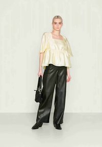 Blusa de cetim amarelo pálido com decote quadrado e design em camadas, combinada com calças largas de imitação de couro preto de cintura alta.