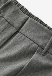 Graue Hose mit elastischem Bund aus strukturiertem Stoff und klaren Linien. Merkmale sind Falten und eine glatte Oberfläche. Keine sichtbaren Beschläge.