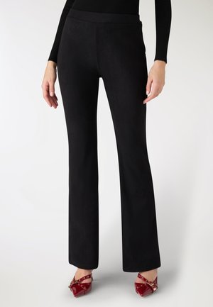 Pantaloni neri a zampa d'elefante realizzati in un tessuto liscio e morbido con vita aderente. Indossati con scarpe con tacco rosse dotate di cinturini e dettagli dorati.