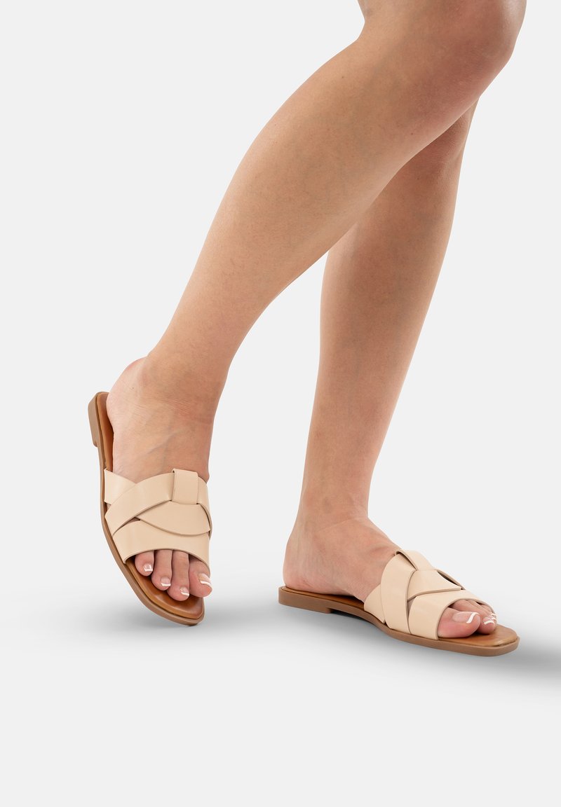Beige flade sandaler med krydsede stropper, lavet af glat syntetisk materiale. Designet med en flad sål og åben tå for åndbarhed.