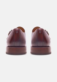 Une paire de chaussures habillées en cuir marron poli avec des talons empilés, vue de l'arrière sur un fond blanc.